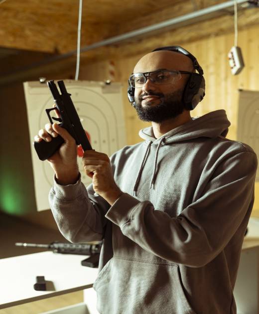 Portrait of shooting range client wearing protection glasses and headset reloading handgun, preparing to shoot targets. Middle Eastern man at indoor shooting ground facility loading pistol